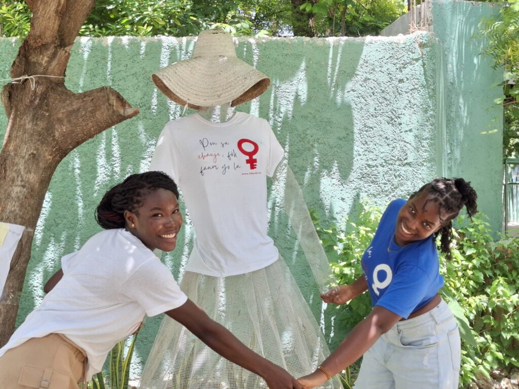 Photo où Daïsha et Juliette se tiennent la main et celles du mannequin de L'Astrée. Les 3 portes des t-shirts Fòk Yo La.